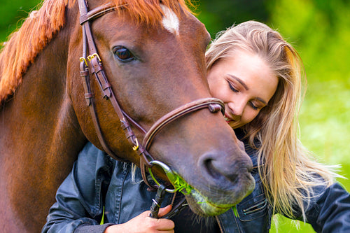 Beautiful woman feeding her arabian horse with grass in the field