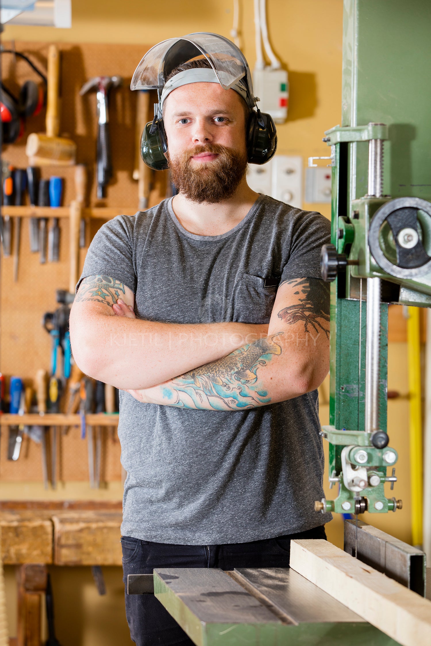 Smiling craftsman with safety mask and earmuffs in workshop
