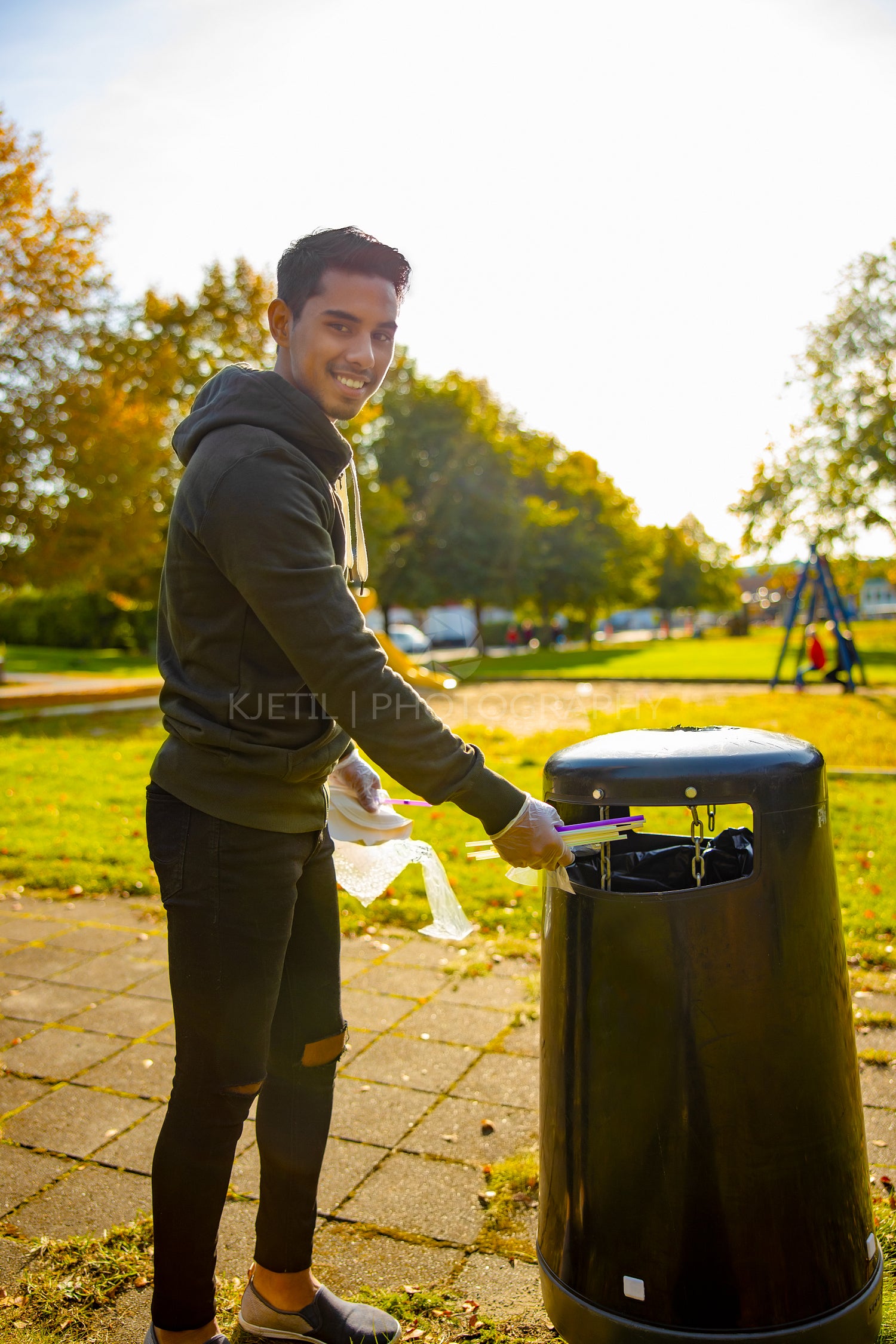 Smiling young volunteer putting straws in garbage bin at park