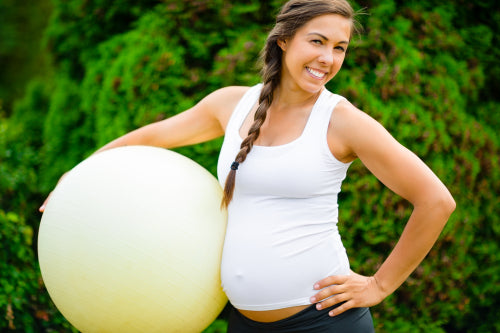 Confident Expectant Female With Exercise Ball Standing In Park