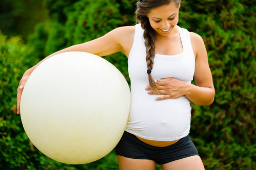 Pregnant Woman Touching Belly While Holding Fitness Ball In Park