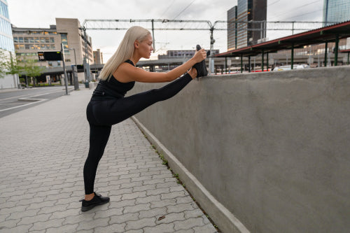 Focused Young Woman Stretching Leg On Railing In City