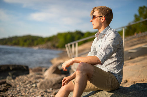 Thoughtful Young Man Sitting On Rock Looking At Sea