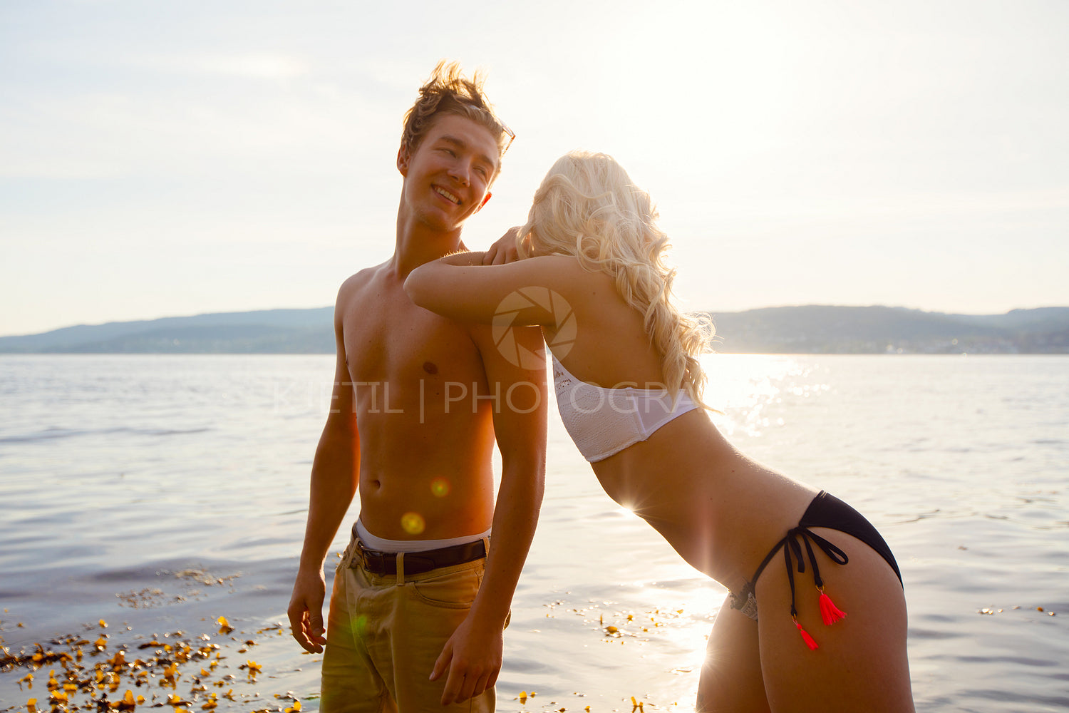 Smiling Young Couple Standing At Beach Against Sky