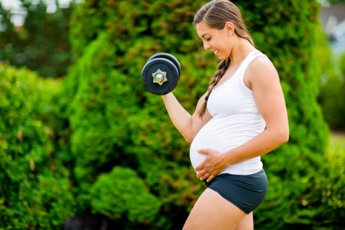 Expectant Mother Touching Belly While Lifting Dumbbell In Park