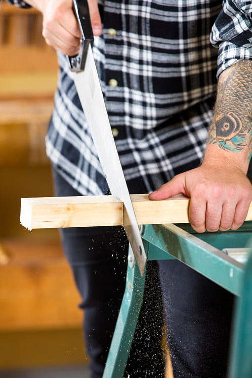 Close-up of carpenter sawing wood with hand saw