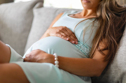 Mid-section of pregnant woman sitting in sofa with her hands at belly