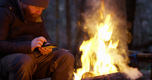 One man using compass and smart phone by campfire in the forest