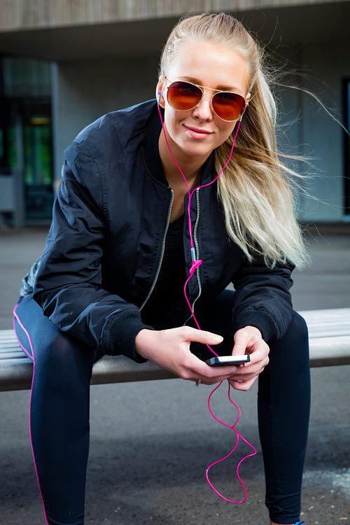 Smiling woman with sunglasses sits outdoor and uses phone