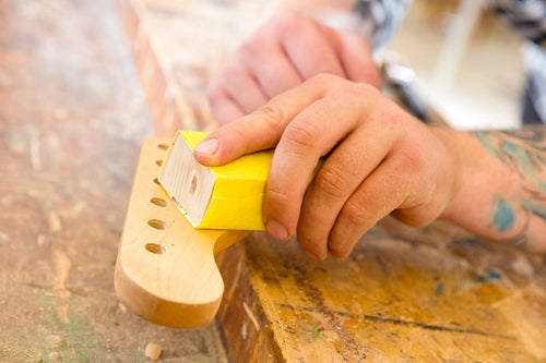 Carpenter sanding a guitar neck in wood at workshop
