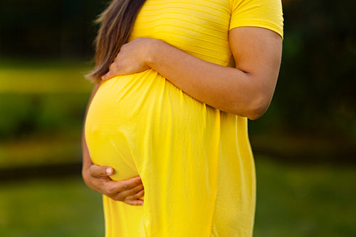 Pregnant woman in bright yellow dress in a garden