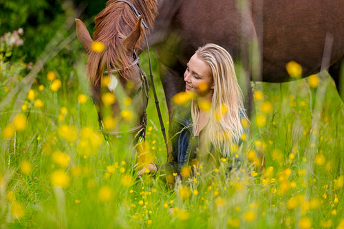 Smiling woman sits in the meadow with her beautiful arabian horse