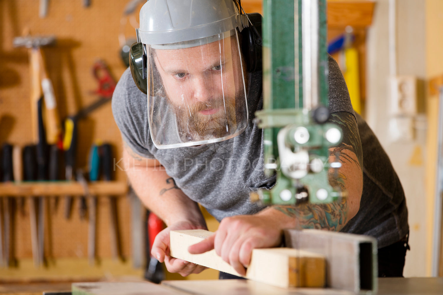 Craftsman with safety mask visor handles band saw in workshop