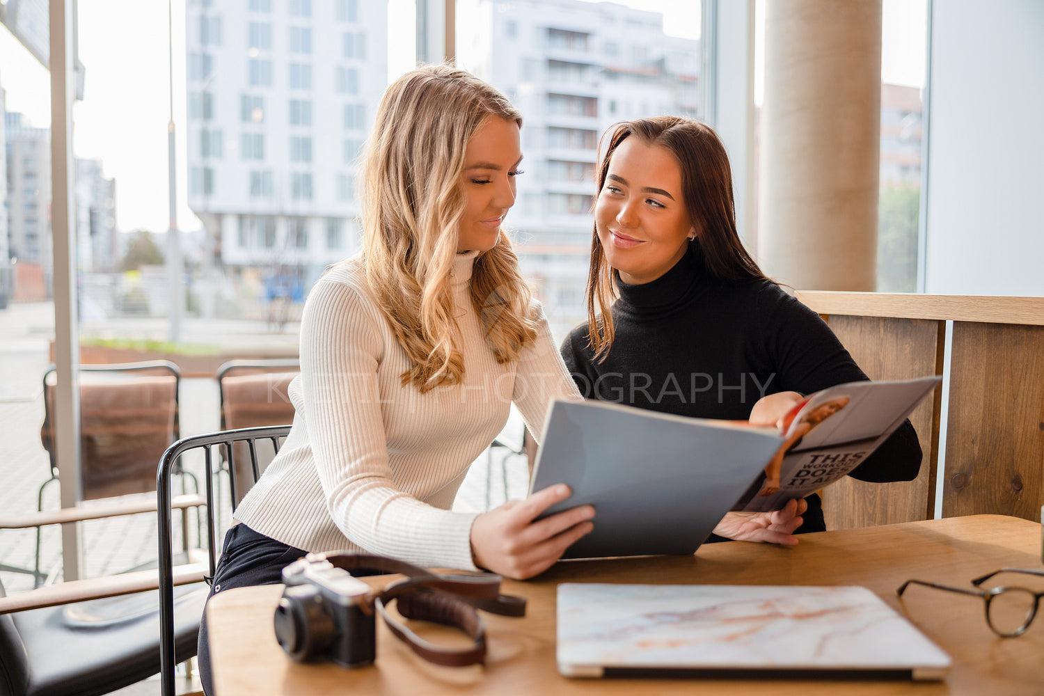 Young Female Blogger Colleagues Discussing Over Magazine At Restaurant
