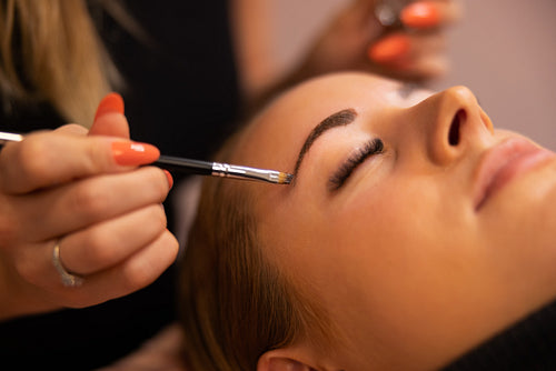 Hands Of Cosmetologist Applying Dye On Female Client's Eyebrow