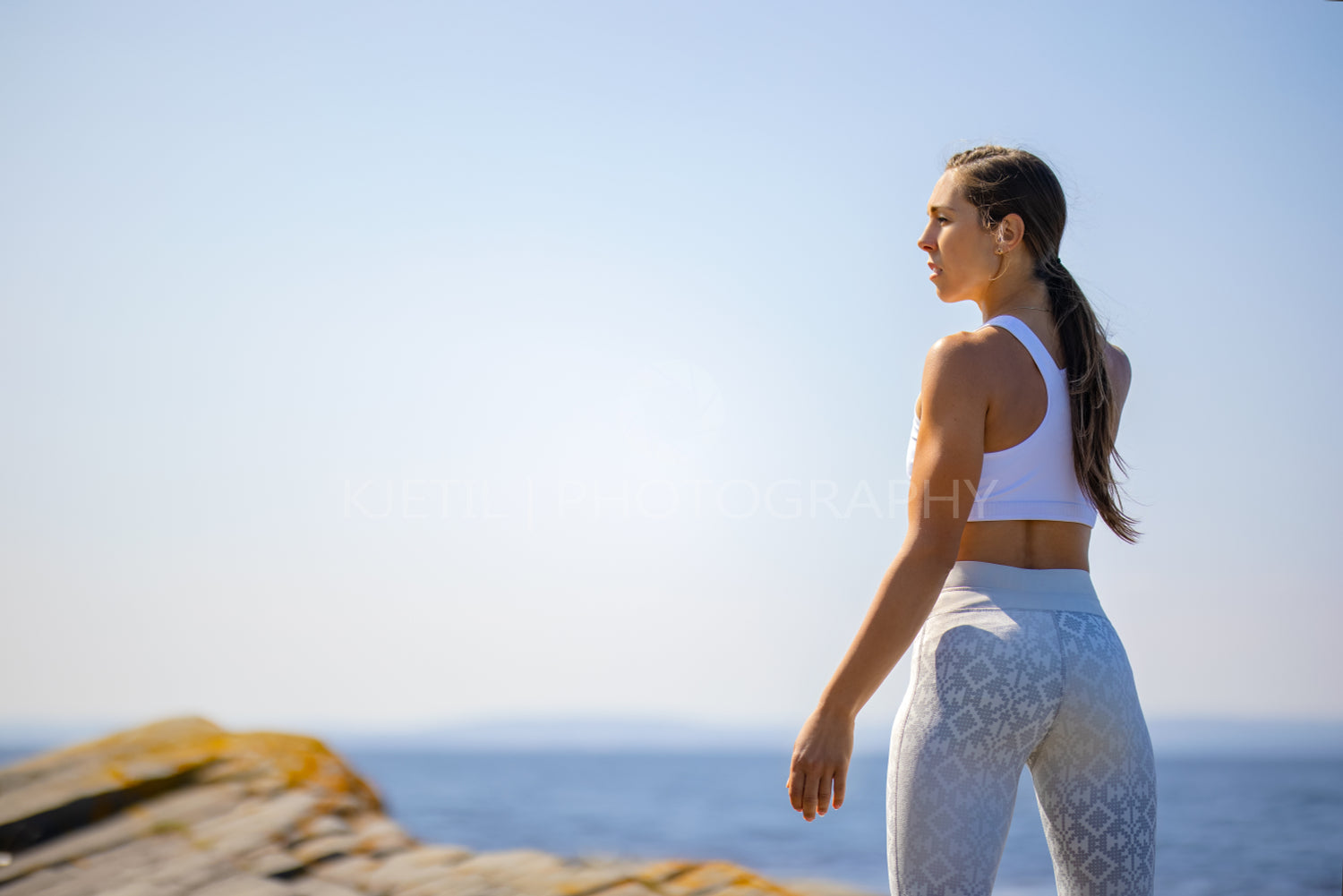 Rear view of female athlete resting after workout against clear sky and sea on sunny day