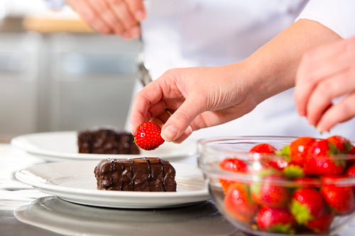 Chefs decorates dessert cake with chocolate sauce in kitchen