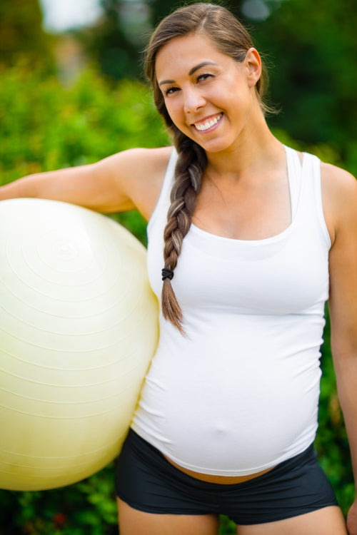 Smiling Young Expectant Mother Holding Fitness Ball In Park