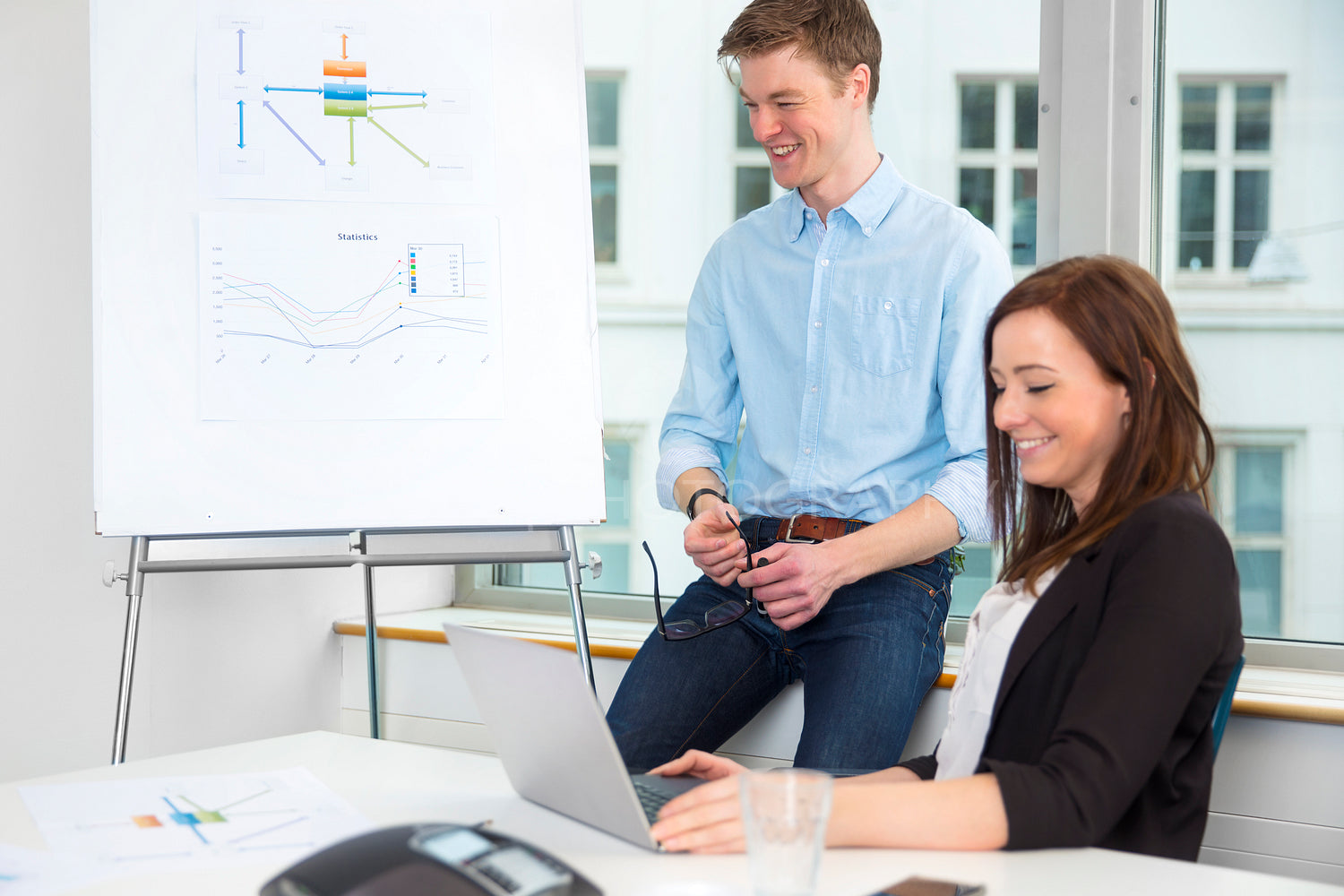 Businessman Smiling By Flipchart While Female Colleague Using La