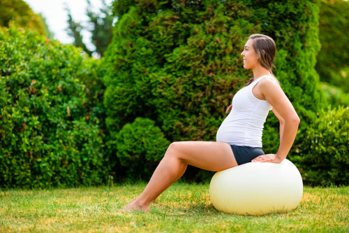 Pregnant Woman Sitting On Yoga Ball In Park