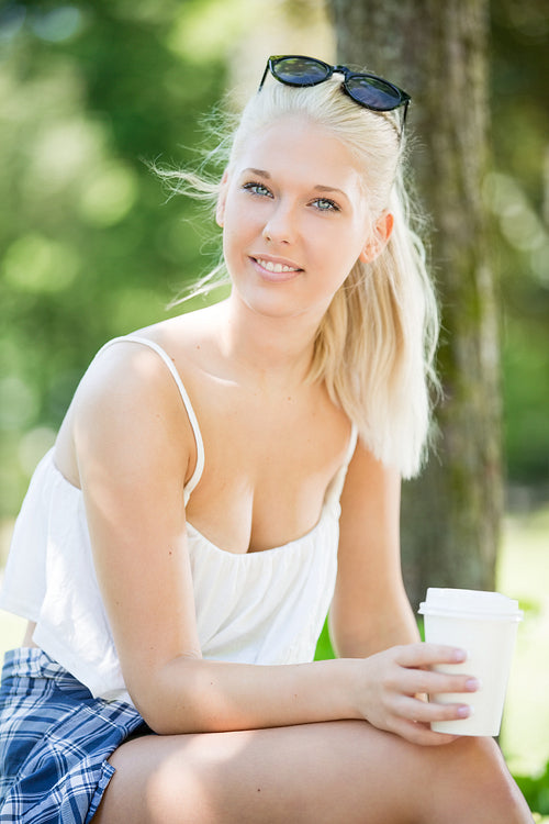 Smiling attractive girl drinking coffee in park