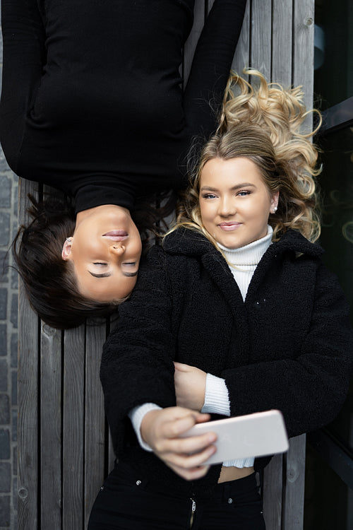 Smiling Friends Lying On Bench Taking Selfie Together in City