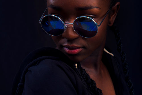 Close-up of woman with dark skin wearing round sunglasses