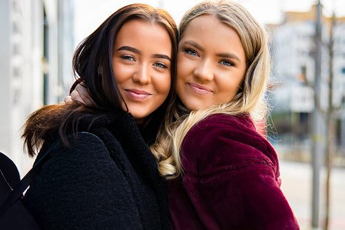 Close-up Portrait Of Two Smiling Friends Embracing In City