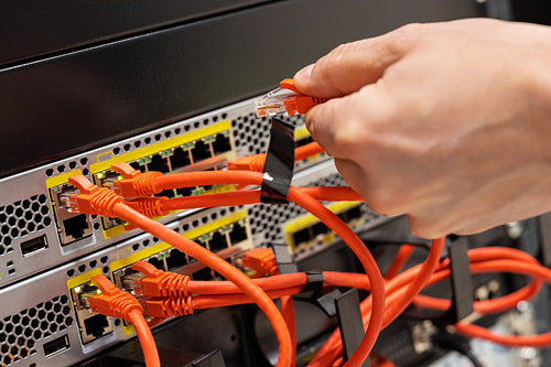 Male IT Engineer Plugging Network Cable In Router in Datacenter