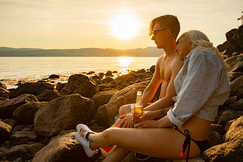 Couple relaxing and drinking beer at the beach at sunset