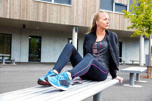 Sporty Woman Listening To Music While Sitting On Bench