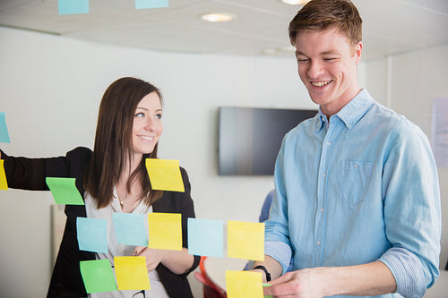 Colleagues Smiling While Discussing Over Notes Stuck On Glass