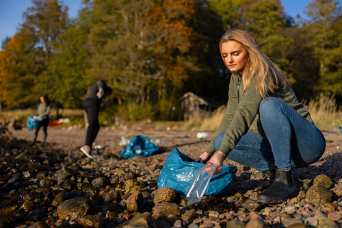 Serious young woman in environment conservation team picking up plastic at beach