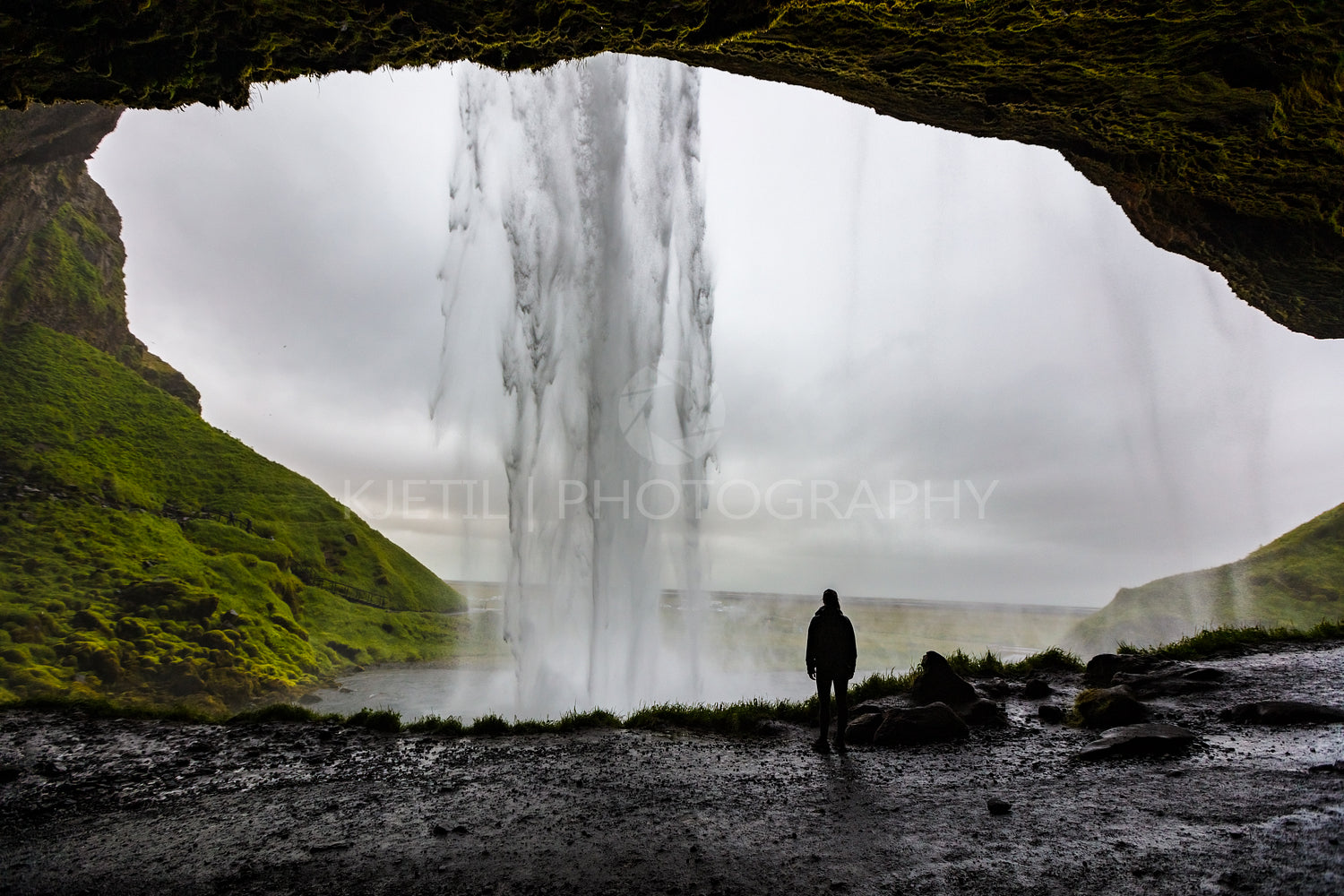 Female hiker looking at Seljalandsfoss waterfall inside a cave