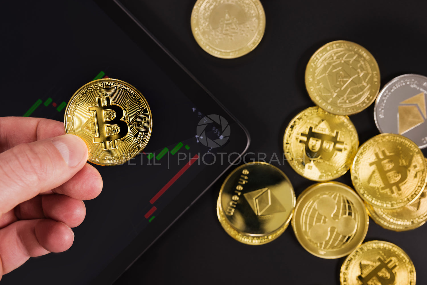 Hand holding Bitcoin over digital tablet by coins