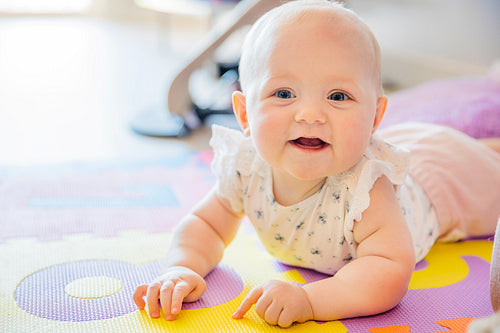 Smiling baby girl with blue eyes playing on floor mate