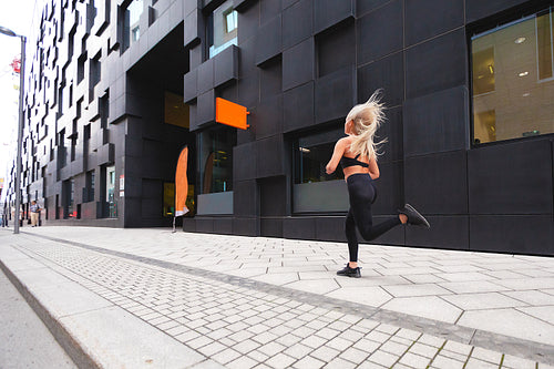 Sporty young woman running fast in minimalist urban environment