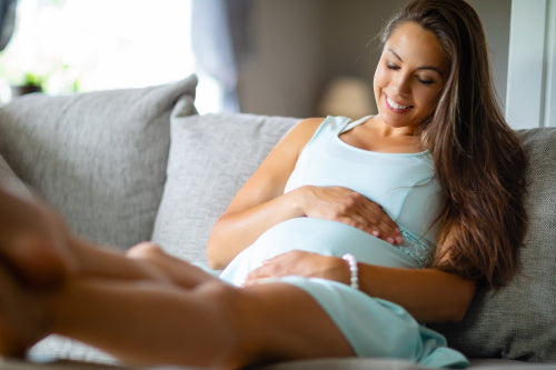 Positive pregnant woman in dress lying on the sofa home