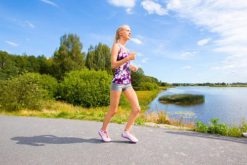 Sporty young woman runs on road along the water