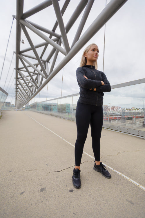Confident Woman in Black Workout Wear Standing At Modern Bridge In City