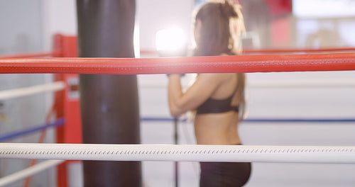 Young female boxer resting with her arms on the ring ropes
