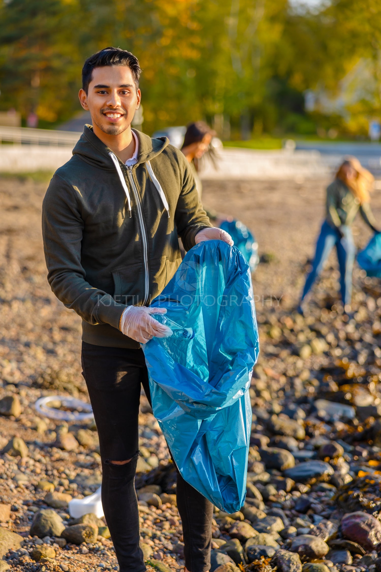 Young man collects garbage in bag with group of volunteers on sunny day