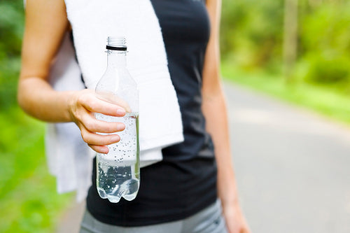 Woman stands outdoor and drinks water after workout