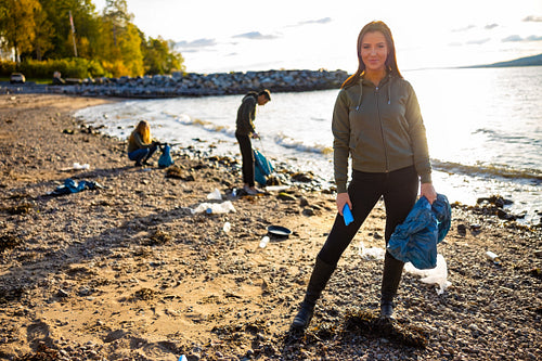 Young woman cleaning beach with volunteers during sunset