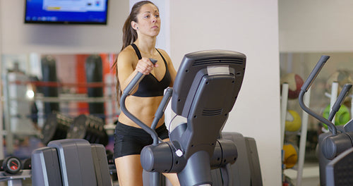 Focused woman training on ellipse exercise machine in fitness gym