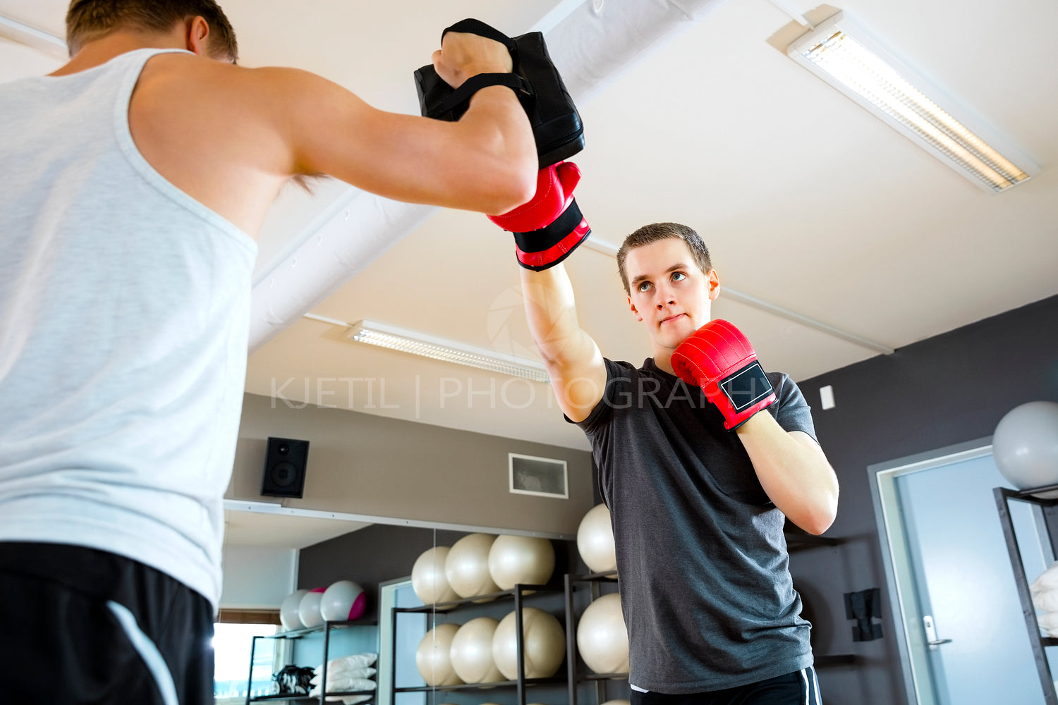 Male Boxer Punching Bag Held By Instructor In Gym