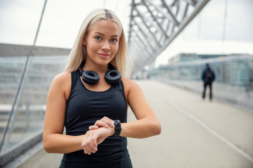 Female Urban Jogger Checking Smartwatch Tracker On Bridge