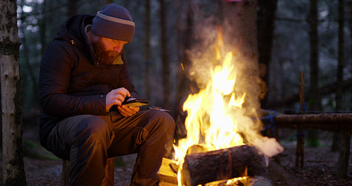 Man using compass and smart phone by campfire in the woods