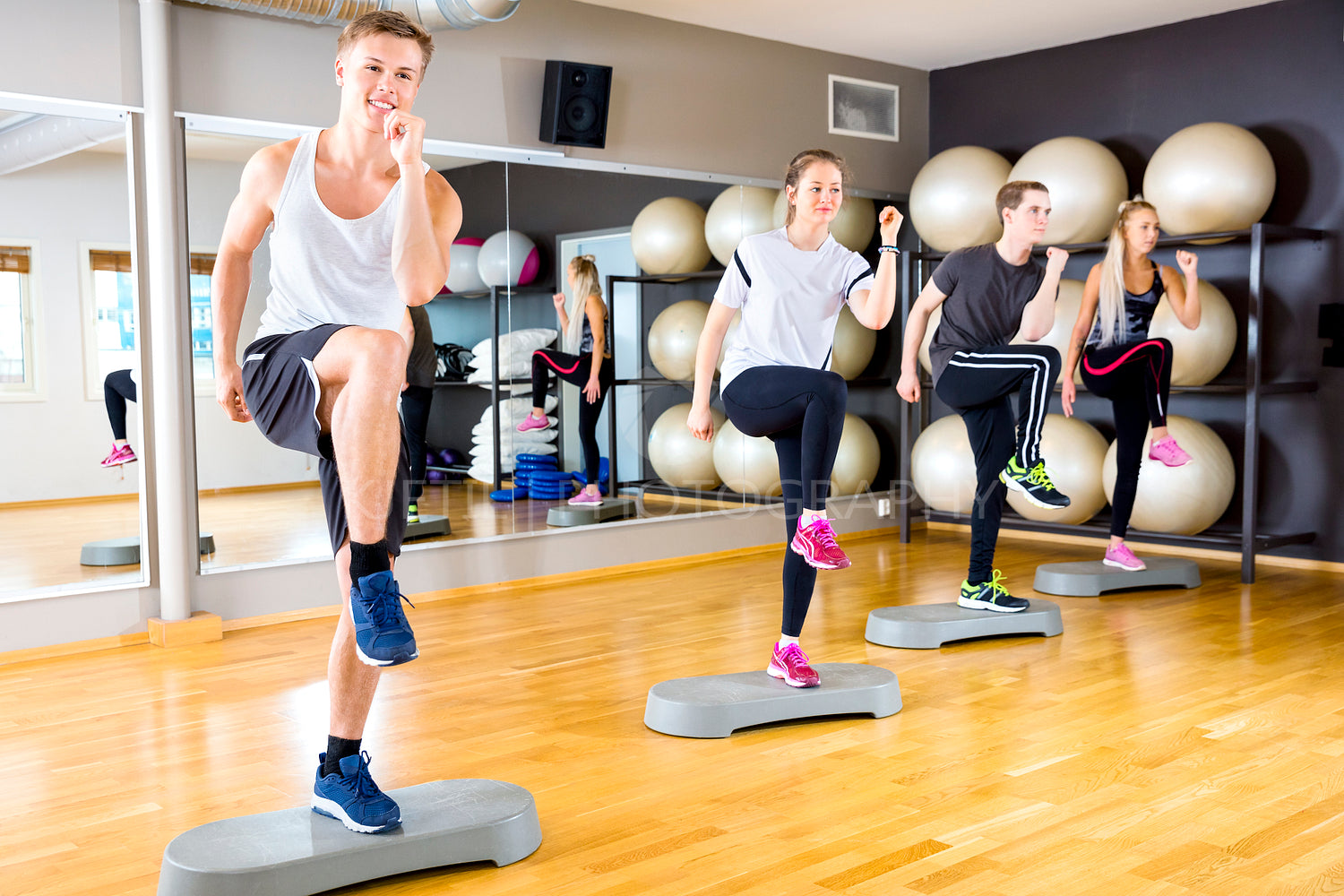 Smiling group raising legs on step platforms at fitness gym