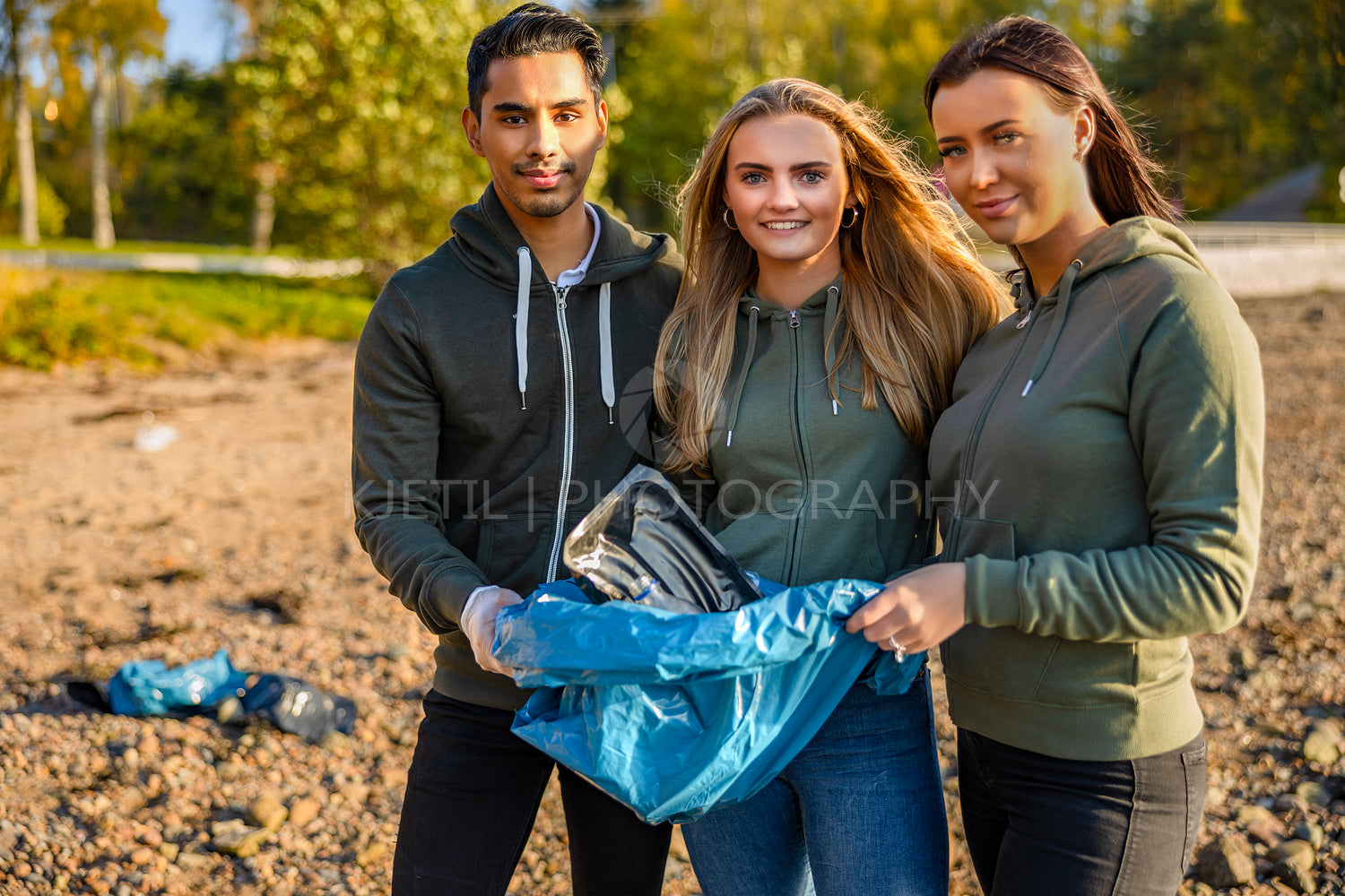 Smiling team of volunteers holding garbage bag at beach